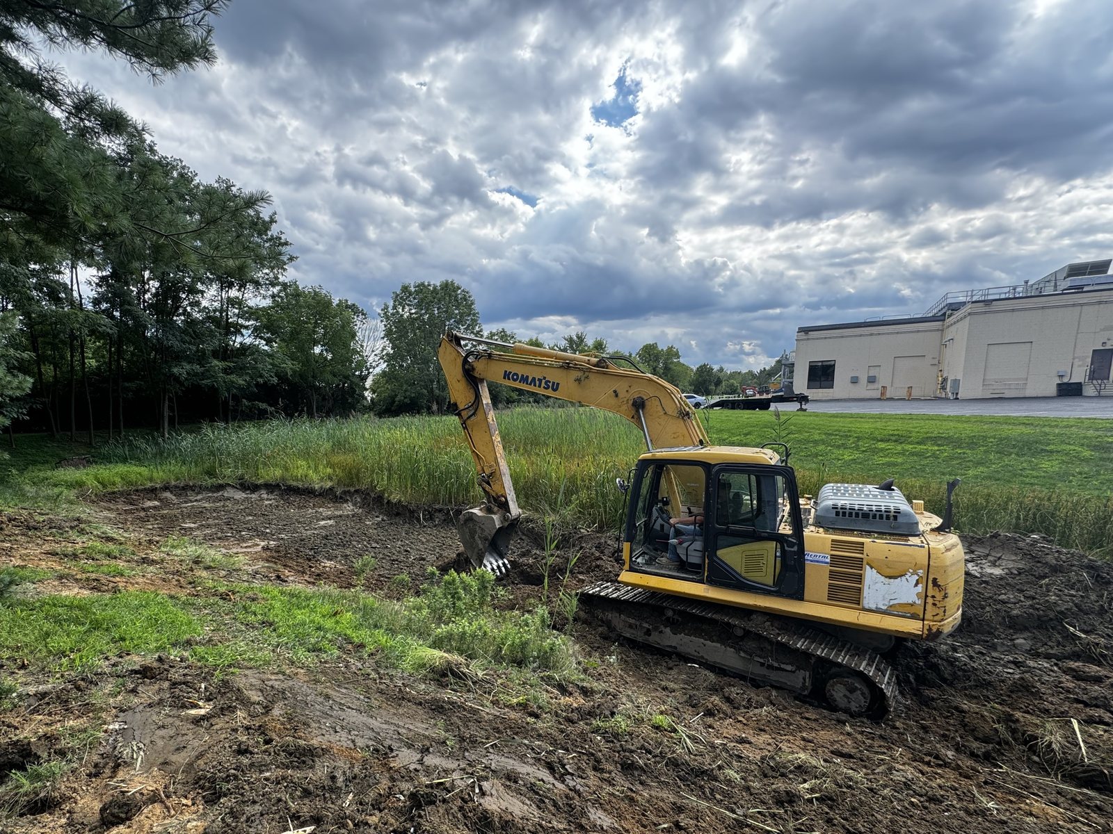 Excavator grading and clearing drainage along the edge of a commercial building lot