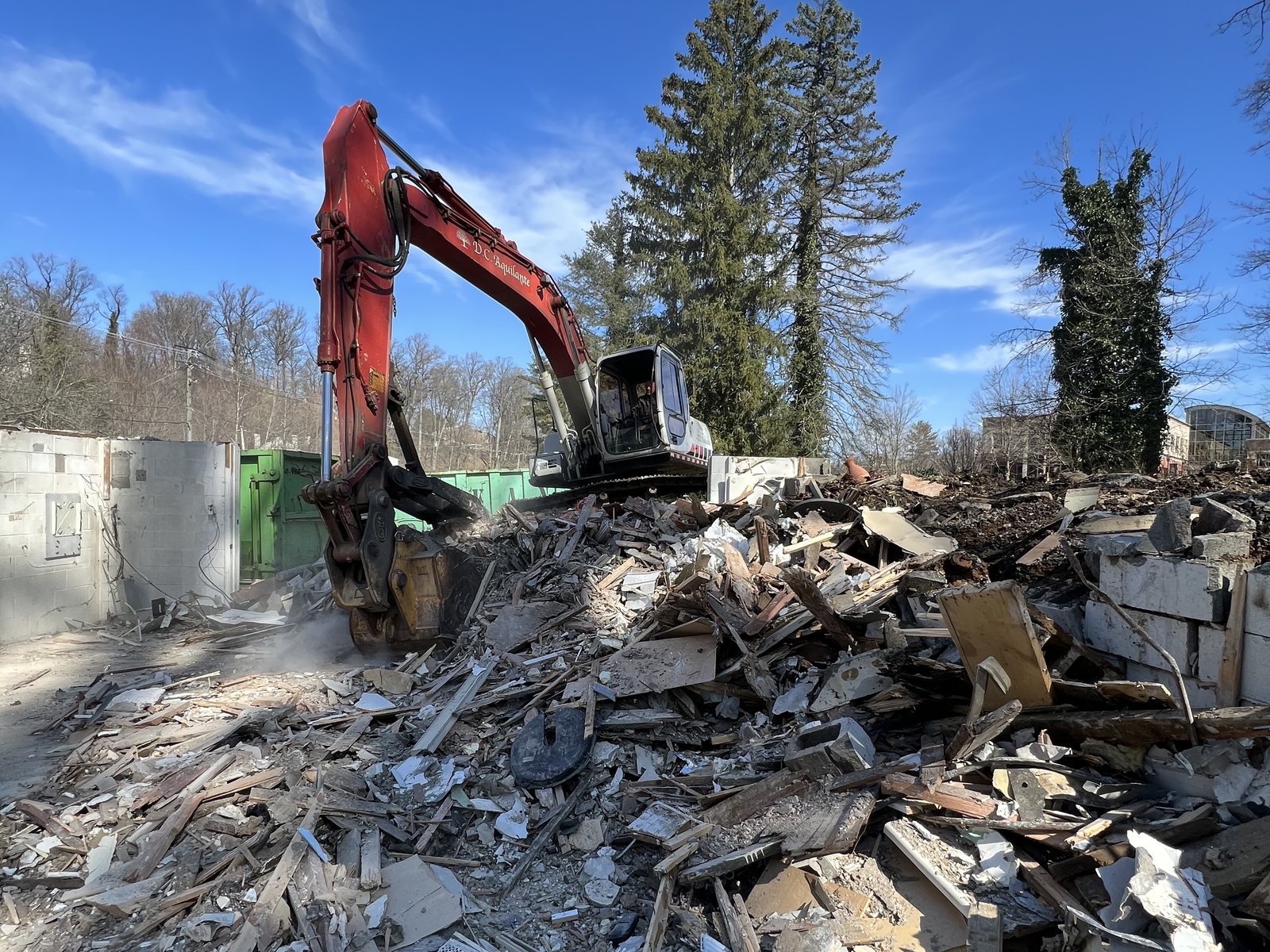 Excavator sorting demolition debris into containers on a cleared building site