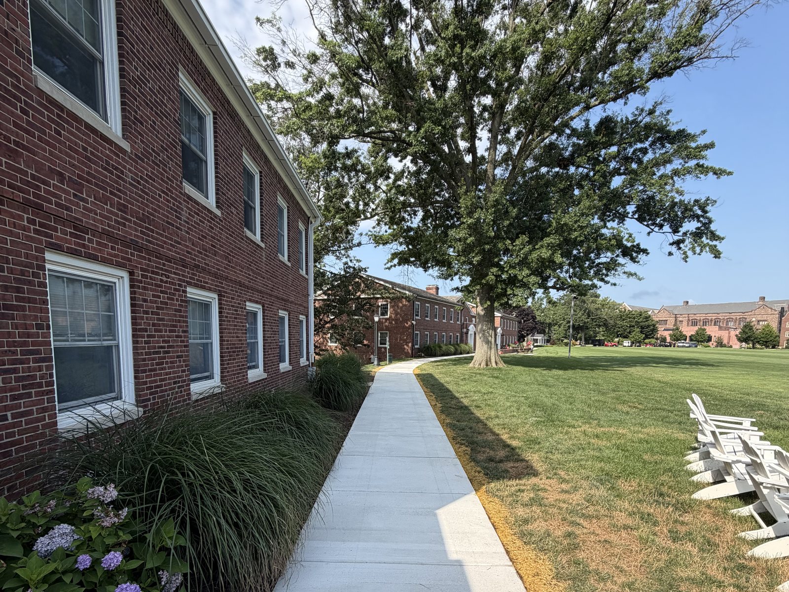Maintained grounds alongside a brick campus building — edged concrete walkway, mulched beds and ornamental plantings